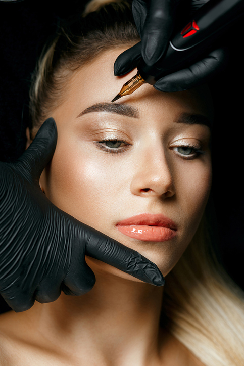 Beautician hand doing eyebrow tattooing on a female brows. Closeup shot